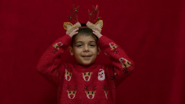 Preschool boy with reindeer horns in christmas ugly sweater explaining something and showing thumbs down. slow motion. High quality 4k footage