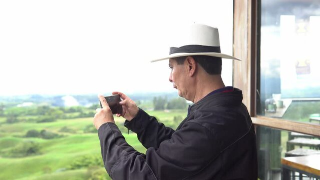 A coffee grower taking pictures with his cell phone on a lookout point