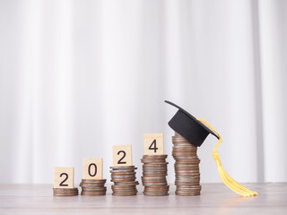 Study goals, Wooden block with number 2024 on stack of coins with graduation hat. The concept of...