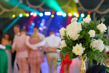 Bride's wedding bouquet and dancing couples at the wedding reception in the background - 689727564