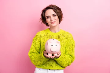 Fotobehang Photo of young girl collect in pig bank earn coins for future studying in european expensive university isolated on pink color background © deagreez