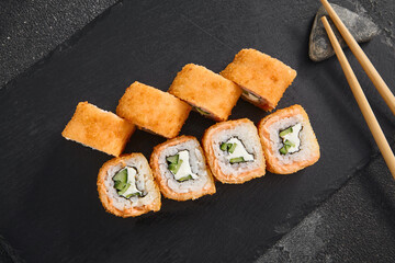 Golden Philadelphia tempura roll filled with salmon, cucumber, and cream cheese, presented on a textured black slate