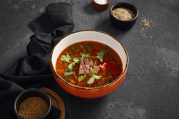 Authentic Georgian Harcho soup, rich with beef and fresh cilantro leaves, served in a rustic orange bowl on a dark grey surface.