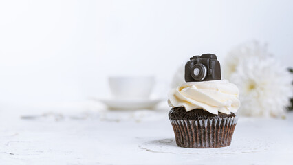 Cupcake decorated with a miniature chocolate camera, close-up with selective focus. Holiday greetings concept, banner with copy space for text