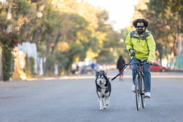 Young Latino man with sunglasses riding a bicycle with his husky dog