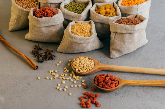Shot of small bags with colorful cereals, nutritious legumes, star anise near, two wooden spoons with red goji berries. Raw products