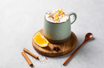 Mug of hot chocolate with whipped cream and orange zest on a wooden board on a light  background with a cinnamon sticks, spoon and fresh orange slices.