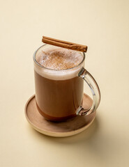 Glass cup of hot chocolate with whipped cream and cinnamon stick  on a yellow background.
