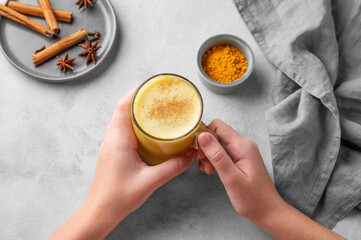 Hands holding turmeric golden milk latte with spices and honey. Detox, immunity boosting,...