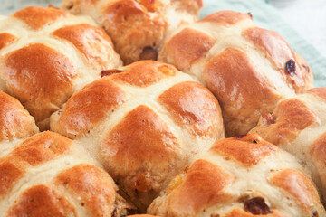 Easter Hot cross buns. Traditional Easter treats cross buns with raisins, butter, chocolate candy eggs with blossoming cherry or apple flowers on rustic light wooden backgrounds. Easter holiday meal.