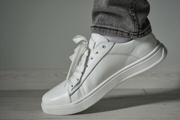 one foot is wearing a white sneaker,stylish fashionable sneakers on the leg with gray jeans