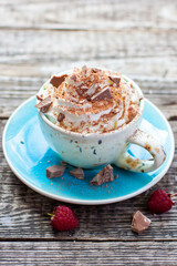 A beautiful blue cup of coffee with whipped cream, cocoa powder and raspberries on rustic wooden background