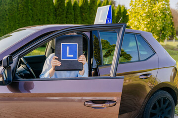 Happy young female driver showing her L sign learner driving school in Europe, driving school novice driver concept.