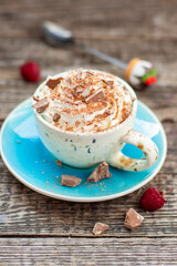A beautiful blue cup of coffee with whipped cream, cocoa powder and raspberries on rustic wooden background