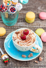 A beautiful blue cup of coffee with whipped cream, cocoa powder and raspberries on rustic wooden background