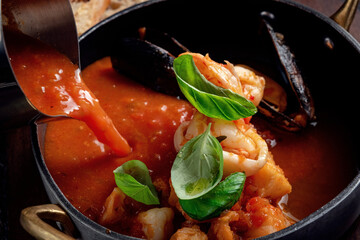 Italian tomato soup with seafood is poured into an iron bowl