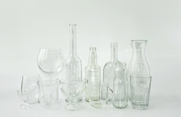 On a light background on the table there is a variety of clean, transparent glassware, bottles, jars, glasses, shot glasses, glasses.  Zero waste concept, glassware.  Foreground, background.