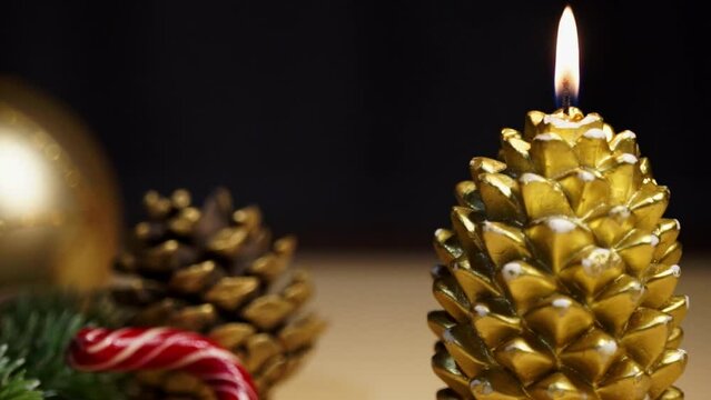 A New Year's candle in the shape of a golden cone burns on a festive table next to Christmas decorations	
