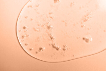 Close up smear of transparent cosmetic product with bubbles on a peach background. Texture and background. Color of the Year 2024