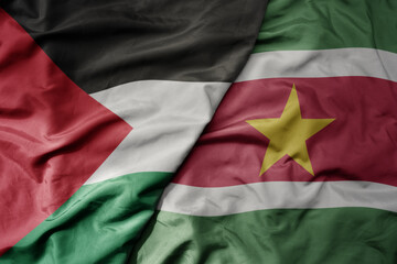 big waving national colorful flag of suriname and national flag of palestine .
