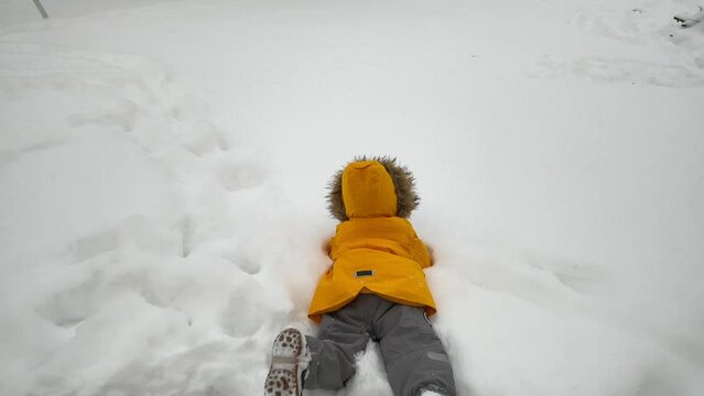 happy child playing on the snowy yard of a house in winter falling into the snow