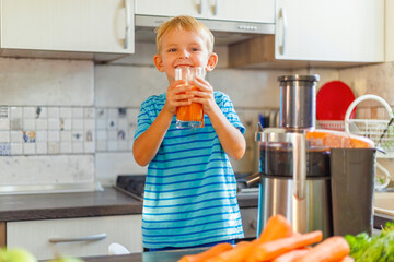 Little boy drinking freshly squeezed carrot juice from a glass in the kitchen
