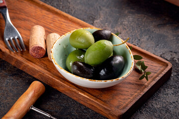 Large green and black olives in a bowl on a wooden board. Fresh extra virgin olives for snacks.