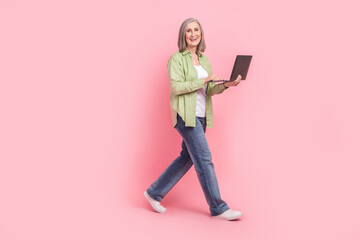 Full length photo of positive successful pensioner woman dressed stylish clothes carry wireless netbook isolated on pink color background