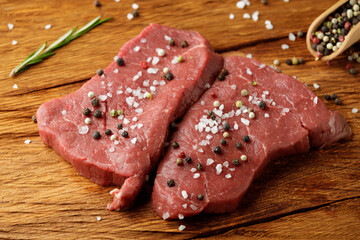 Raw piece of meat black angus steak with rosemary on wooden table