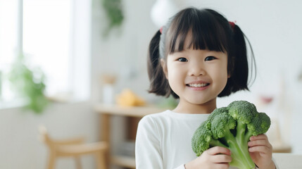 Little beautiful asian girl posing with broccoli in the kitchen. Healthy vegan baby foods concept.