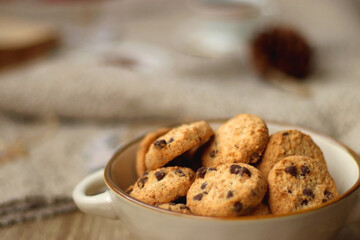 Bowl of cookies, cup of tea, dry oranges, pine cones, books, reading glasses, small presents, various Christmas decorations and lit candles on the table. Cozy Christmas hygge. Selective focus.
