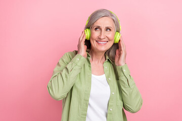 Photo of cheerful dreamy lady wear green stylish clothes hands touch mp3 player look up offer empty space isolated on pink color background