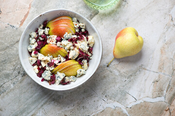 Bowl of salad with radicchio, pear and blue cheese, above view on a light-grey granite background, horizontal shot