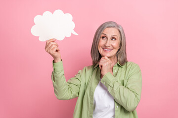 Photo of nice minded senior lady wear green trendy outfit hand touch chin hold cloud look up empty space isolated on pink color background