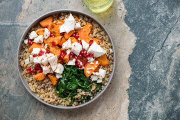 Quinoa with feta, roasted sweet potato, pomegranate and wilted spinach, above view on a beige and...