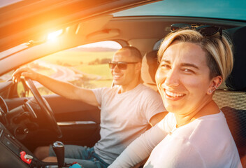 Portrait of cheerful smiling young woman with husband have auto journey inside modern car. Safety...