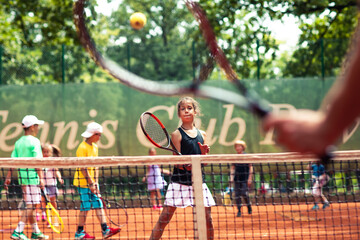 Little child girl playing tennis during practice on clay court