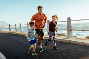 Father running with kids on beach promenade