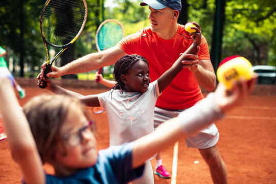 Tennis coach working with little girl on clay court