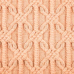 Knitted peach background. Large knitted fabric with a pattern. Close-up of a knitted blanket. Demonstrating the colors of 2024 - Peach Fuzz.