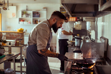 Chef cooking food with fire in pan at restaurant kitchen