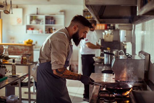 Chef cooking food with fire in pan at restaurant kitchen