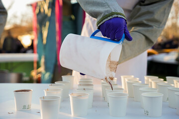 an unrecognizable person with gloves serves hot chocolate at the Three Kings Day celebration