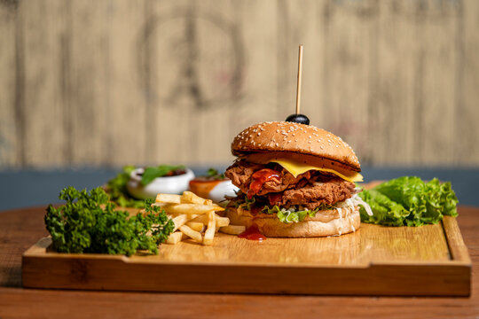 Burger with french fries and vegetables on wooden board, closeup