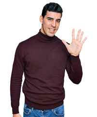 Handsome hispanic man wearing casual turtleneck sweater showing and pointing up with fingers number five while smiling confident and happy.