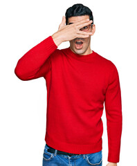 Handsome hispanic man wearing casual clothes and glasses peeking in shock covering face and eyes with hand, looking through fingers with embarrassed expression.