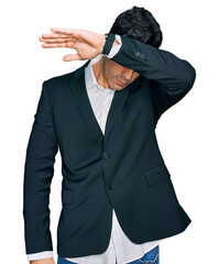 Handsome hispanic man wearing business clothes covering eyes with arm, looking serious and sad. sightless, hiding and rejection concept