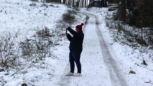  A young woman walks through the winter park and takes photos 
