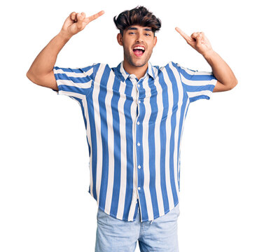 Young hispanic man wearing casual clothes smiling amazed and surprised and pointing up with fingers and raised arms.