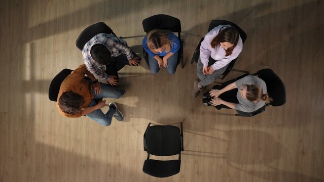 In the shot above a group of people, male and female, are sitting on a chair. They have come to a meeting, a session, therapy. They are discussing something, talking, smiling, waiting for a mentor